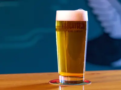 Close up of Pint Glass of Beer at Bobcaygeon Brewing Company  sitting on a wooden table witha  blue background.